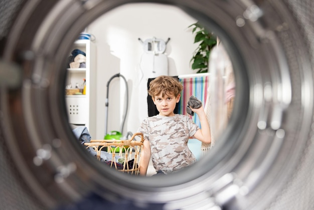 Small cheerful boy interested in the operation of the device puts clothes into the drum