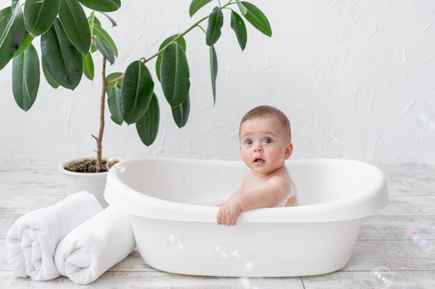 A small child boy 8 months old bathes in a bath with foam and soap bubbles