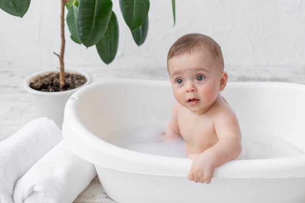 A small child boy 8 months old bathes in a bath with foam and soap bubbles