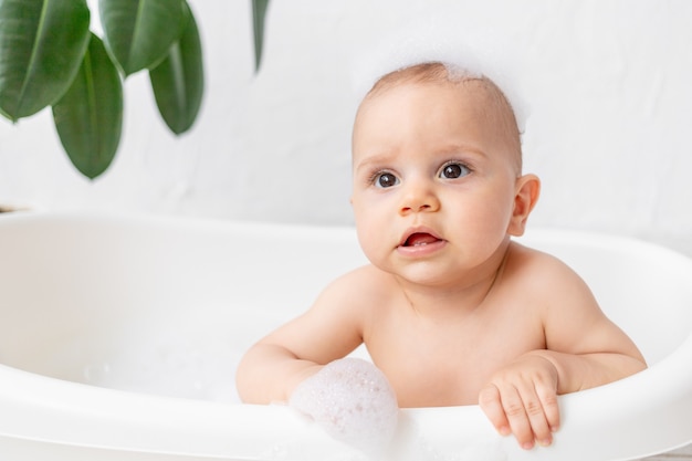 A small child boy 8 months old bathes in a bath with foam and soap bubbles