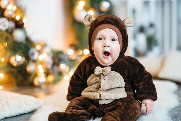 A small child in a brown teddy bear costume sits on the floor