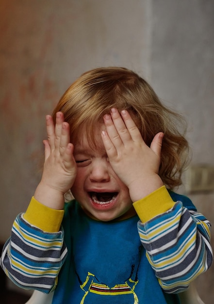 A small child cries closing his eyes with his hands