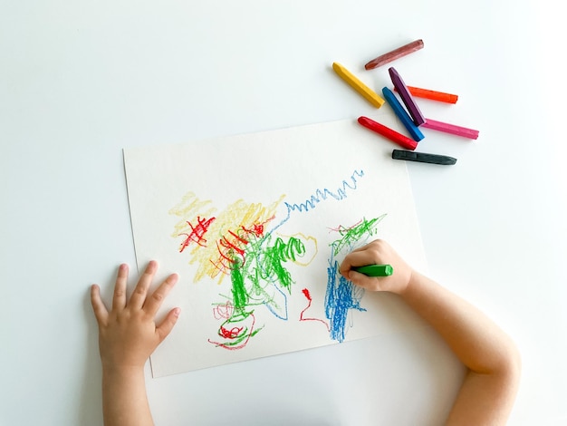 Small child draws with pastel crayons on white table fathers day