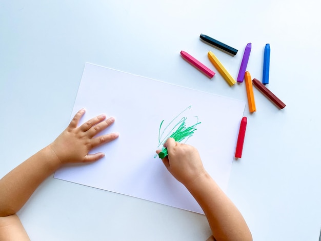 small child draws with pastel crayons on white table High quality photo