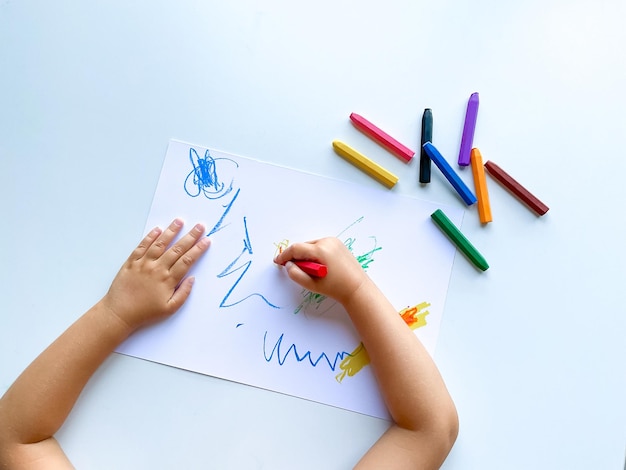 small child draws with pastel crayons on white table High quality photo