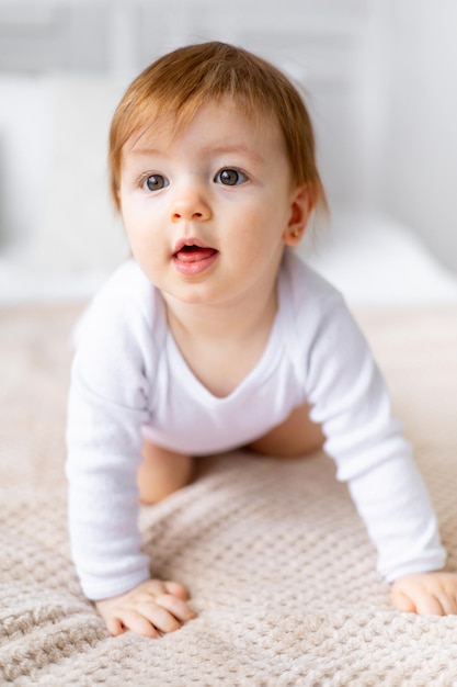 A small child girl learns to crawl on a bed in a bright room on cotton white linen closeup portrait