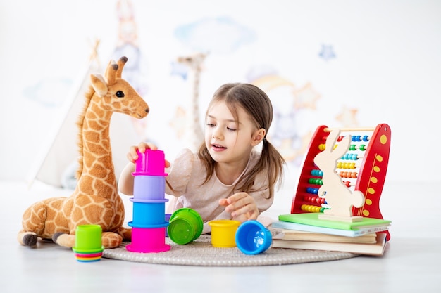 a small child girl plays with toys on a rug in a bright childrens room building a pyramid lying on the floor a smiling child at home playing early preschool development