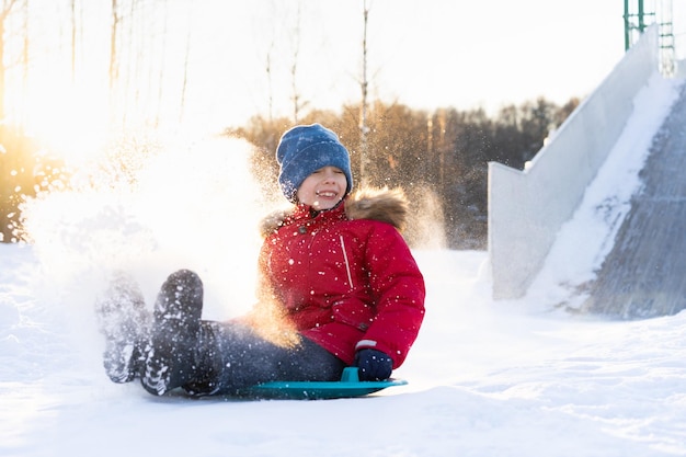 A small child in a red jacket rides down a slide on ice a cheerful child emotions from winter fun