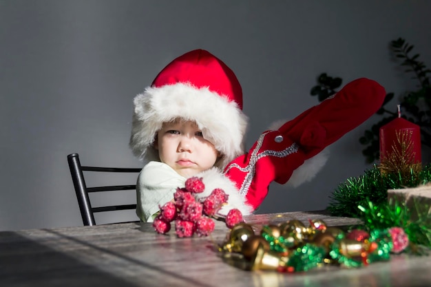 A small child in a santa claus hat and red mittens with christmas gifts is sitting at the new years