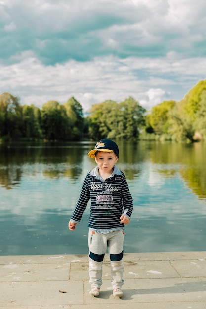 A small child stands near a lake in a park in the summer