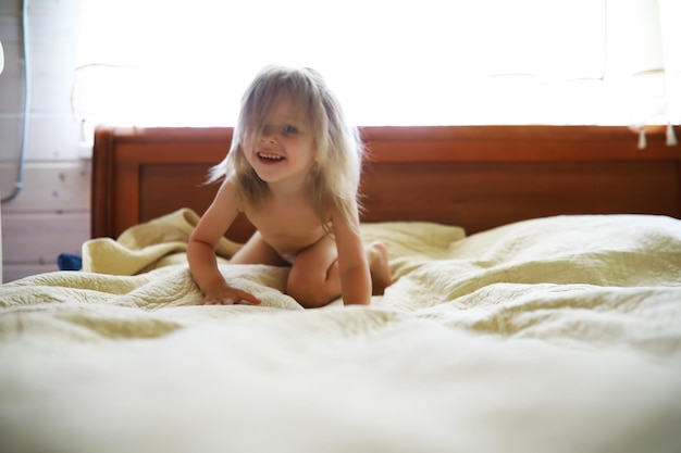 A small child with blond hair lies on the bed Baby girl is playing on the couch