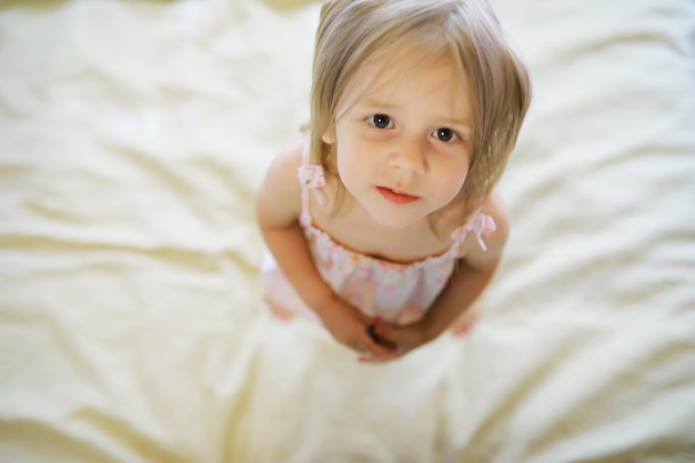 A small child with blond hair lies on the bed Baby girl is playing on the couch