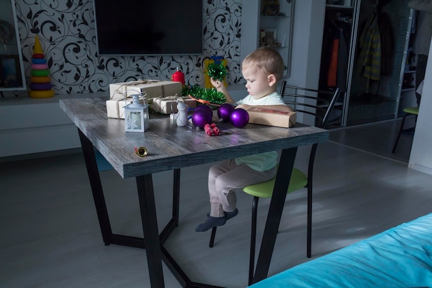 A small child with Christmas gifts is sitting at a New Year's wooden table with a tablet in his hands