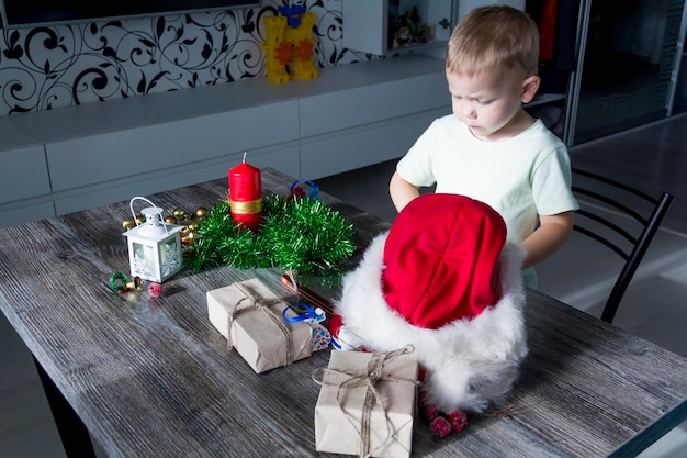 A small child with Christmas gifts is sitting at a New Year's wooden table with a tablet in his hands