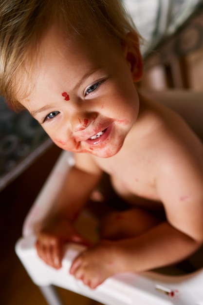 Small child with a dirty face sits on a chair turning to the side