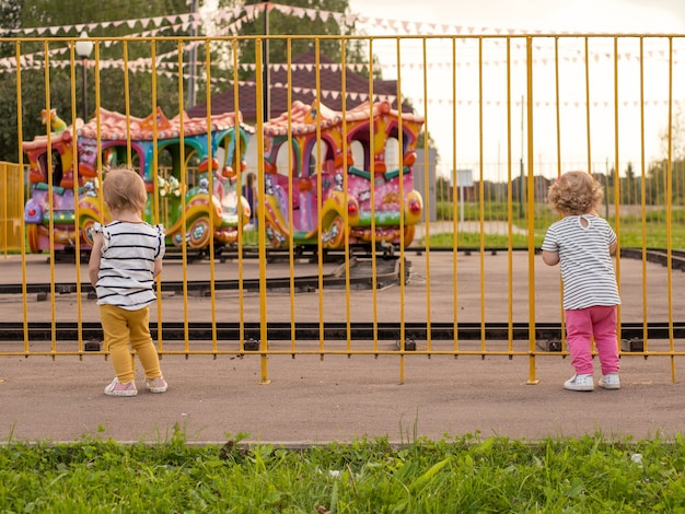 Small children look over the fence at the children's train and dream of a ride