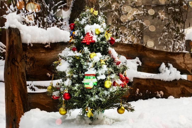 A small Christmas tree decorated with toys gifts bows bells in the snow on the street