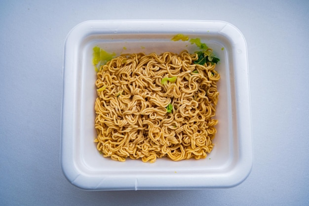 A small container of noodles with a green vegetable on top.