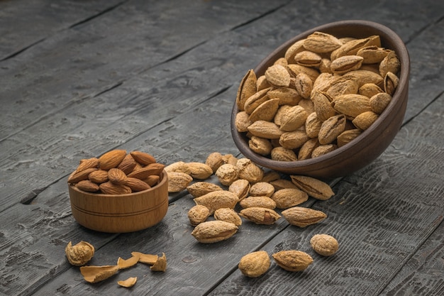 A small cup with peeled almonds and a large clay bowl with unpeeled almonds spilling out. Vegetarian food.