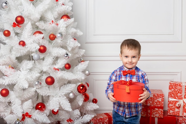 Small cute boy casual dressed standing in white room among christmas decorations