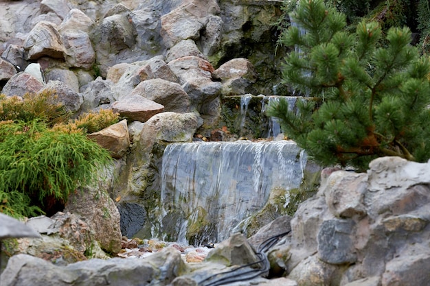 Small decorative river waterfall. Water flows over rocks and stones.