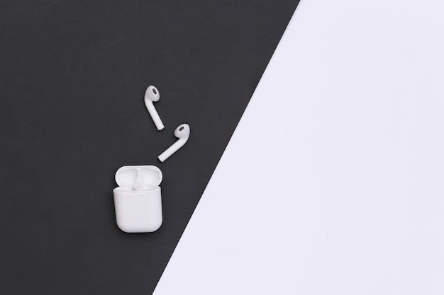 Small earbuds with charger case on black white background. Top view. Copy space