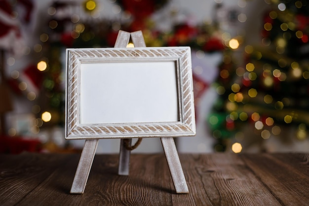 Small easel with framed blank postcard on wooden table with Christmas background Mockup of Christmas card