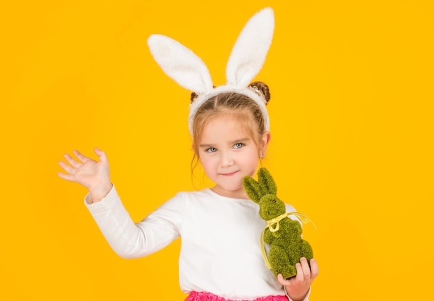 small easter child in bunny ears hold toy on yellow background. hello.