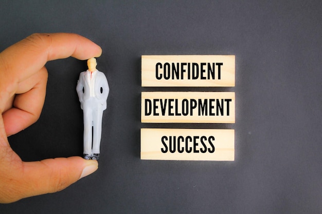 A small figure is standing next to a wooden board that says confidence and development.