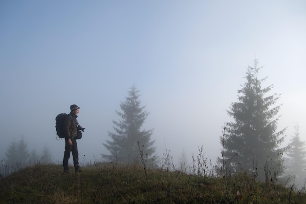 Small figure of lonely hiker enjoying his time on wild forest trail on foggy autumn day