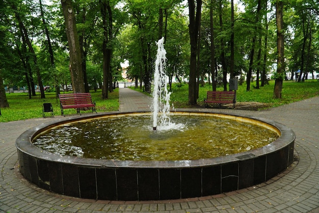 A small fountain and benches around in the city park