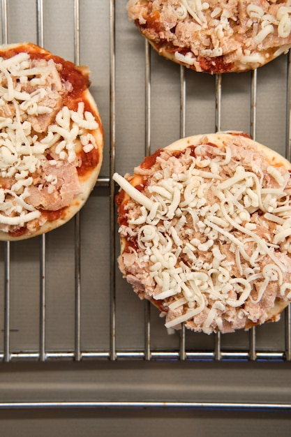 Small frozen pizza semifinished product with tomato sause and cheese on grill prepared for baking