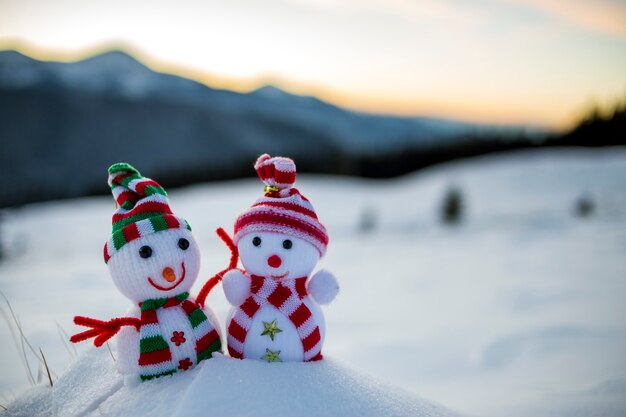 small funny toys baby snowman in knitted hats and scarves in deep snow outdoors on blurred mountains landscape 