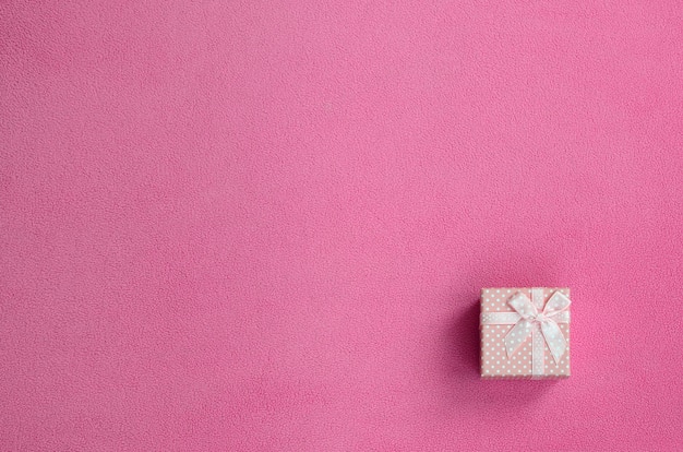 A small gift box in pink with a small bow lies on a blanket of fleece fabric 