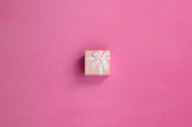 A small gift box in pink with a small bow lies on a blanket of soft and furry light pink fleece fabric. Packing for a gift to your lovely girlfriend