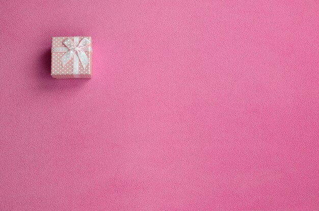 A small gift box in pink with a small bow lies on a blanket