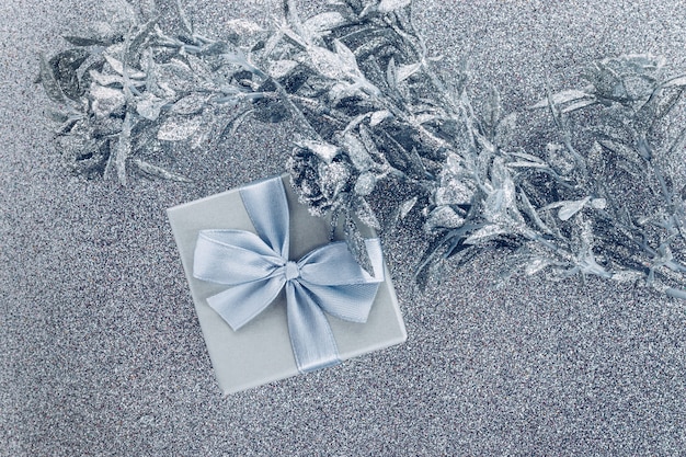 Small gift box with satin bow and artificial silver flowers decoration on silver glitter background