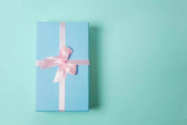 Small gift box wrapped blue paper isolated on pink pastel colorful trendy geometric background Christmas New Year birthday valentine celebration present romantic concept