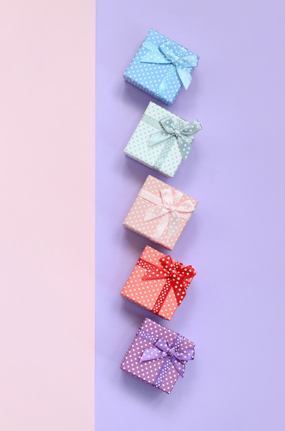 Small gift boxes of different colors with ribbons lies on violet and pink