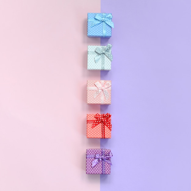 Small gift boxes of different colors with ribbons lies on violet and pink 