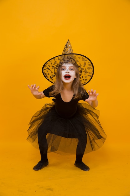 Small girl in Halloween witch costume, orange surface.