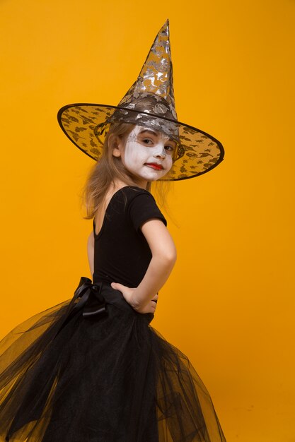 Small girl in Halloween witch costume, orange surface.