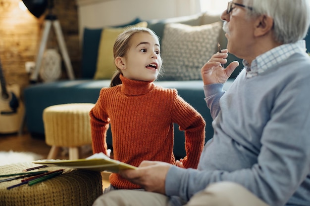 Small girl and her grandfather communicating while drawing at home