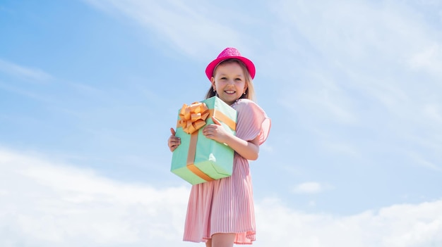 Small girl hold present box little kid with gift box happy birthday party childhood happiness lets celebrate holiday child in summer day on sky background its shopping time