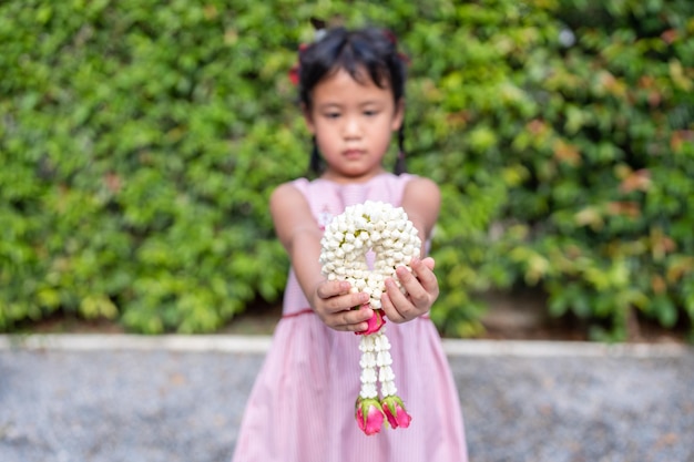 Small girl holding jasmine garland in her hand and gives to her mother on Thai Mother day.