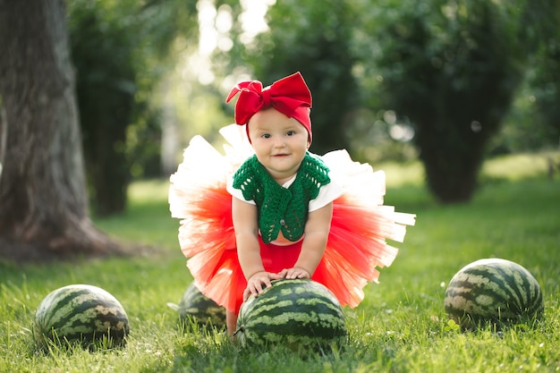 Photo small girl is sitting on the green grass in a red tulle skirt with watermelons.