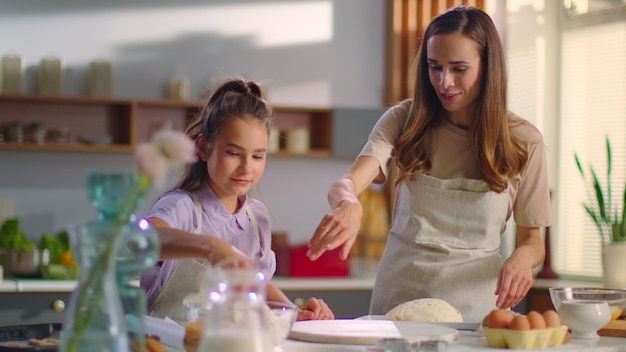 Small girl and woman sprinkling flour on table at modern kitchen Attractive mother and daughter preparing dough for cookies on modern kitchen together in slow motion