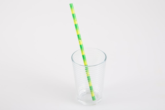 Small glass transparent empty with green straw in carton recyclable cardboard on a grey table background