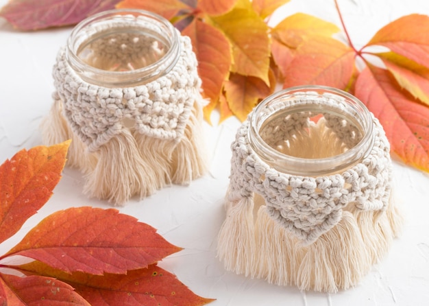 Small glass vases, jars, candleholders with macrame cover. Autumn leaves. Boho