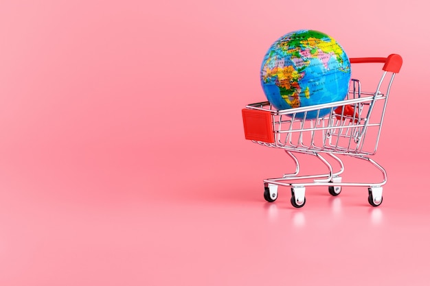 Small globe in a shopping cart on a pink background